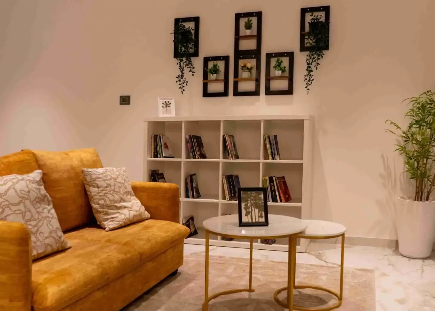 Elegance by Guru Punvaanii, Bidadi, show villa A sunlit living room with a mustard sofa, round tables and a wall of shelves in the Elegance show villa